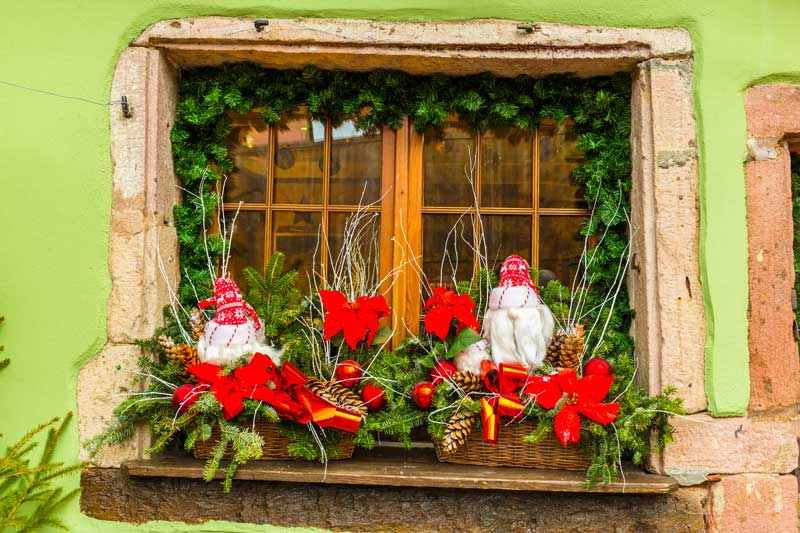 Fenêtre décorée avec guirlande, composition avec branches et pommes de pin, idéal pour Noël.