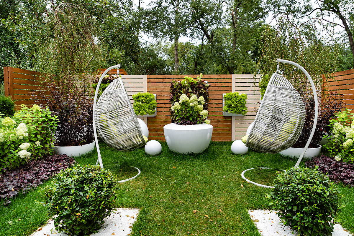 petit jardin avec clôture en bois, 2 sièges d'extérieur et décorations de plantes.