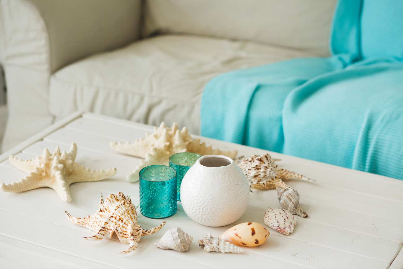 Table basse dans le salon avec des décorations marines, des coquillages et des bocaux turquoise et blancs.