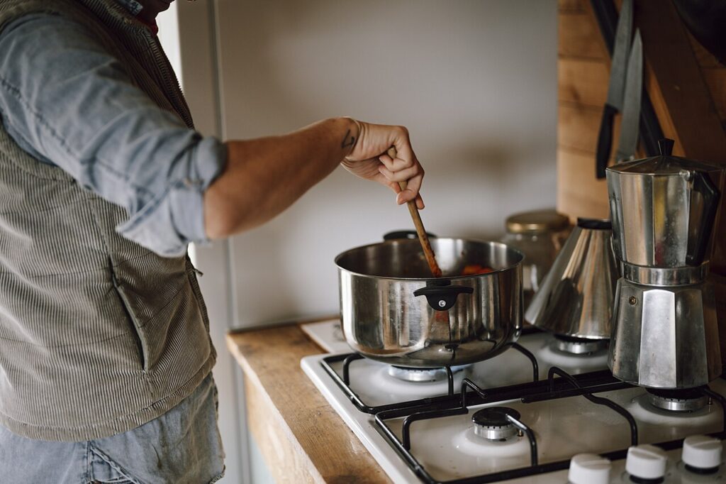 Découvrez le secret caché des vieux citrons - A person stirs a pot on the stove, preparing a warm dish in a cozy kitchen. The space features wooden ac
