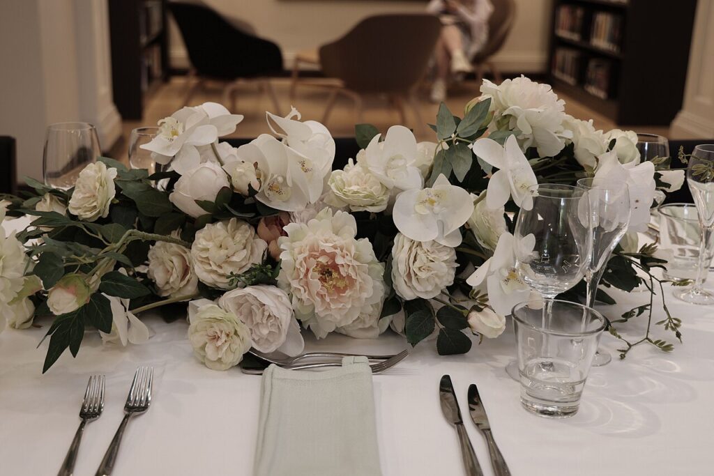 Une cascade de fleurs dans le jardin - Une table de salle à manger élégamment dressée, avec une nappe blanche, des couverts en argent, de la verrerie 